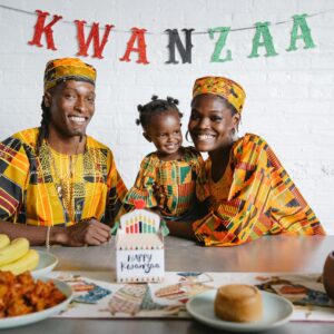 African American family enjoying Kwanzaa indoors with food and traditional clothes, smiling together.